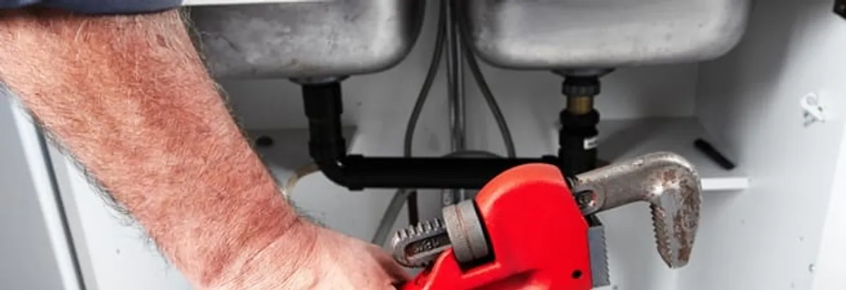 Garbage disposal repair technician tightening drain connections under a kitchen sink in Buffalo, NY