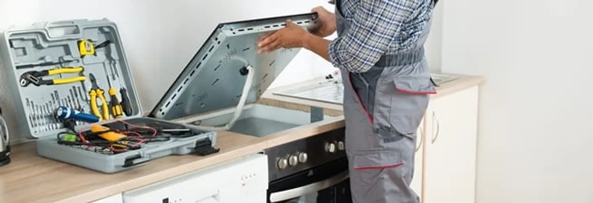 Cooktop repair technician lifting a built-in stovetop for service in Buffalo, NY
