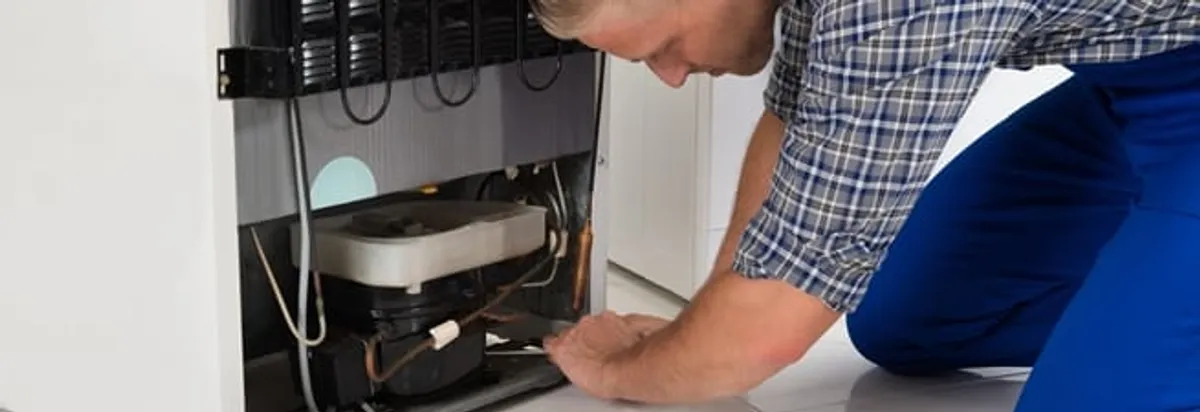 Refrigerator repair technician servicing the compressor and condenser area in Buffalo, NY
